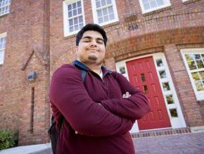 Raj Donepudi stands in front of the red main door at Mauney Hall